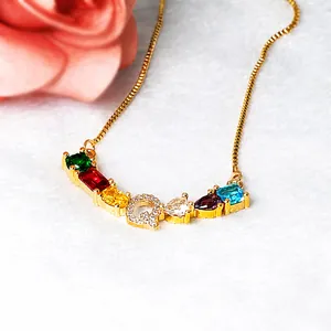 Detalle del collar dorado con piedras preciosas de colores y colgante de letra Q brillante