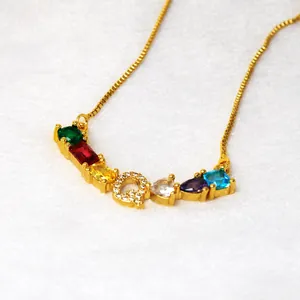 Primer plano del colgante letra Q dorado con piedras preciosas de colores y circonitas