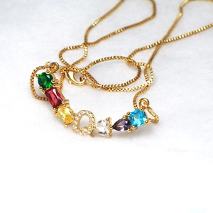 Detalle del collar dorado con colgante de letra Q y piedras preciosas de colores