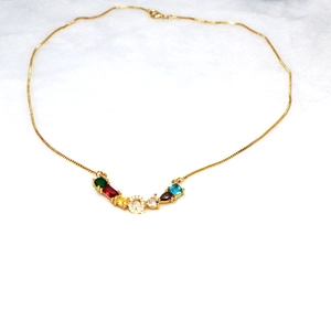 Detalle del collar de cadena dorada con colgante letra Q de circonitas y gemas de colores