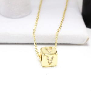 Macro shot of gold cube pendant with zircon V initial and fine cross chain jewelry