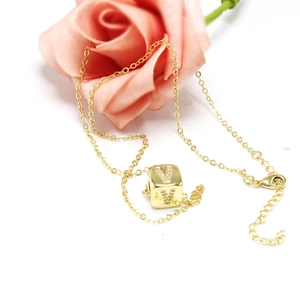 Detail of gold cube pendant with crystal letter V on fine chain against pink roses