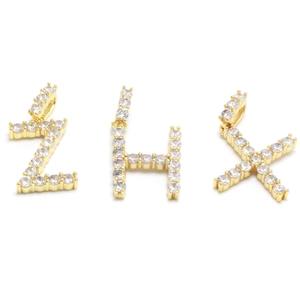 Macro detail of gold-plated Z, H, and X letter pendants with pavé set zircon stones