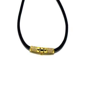 Detail of gold cylinder bead with cubic zirconia inlays and hollow pattern on black rope