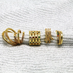 Close-up of four gold-plated ear cuffs with colorful zircons on grey fabric