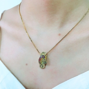 Detalle de un collar bañado en oro con un colgante de zapato con circonitas de colores