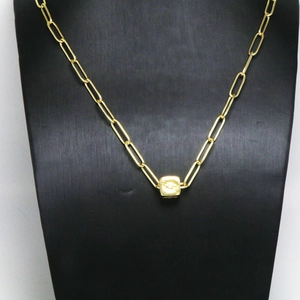 Dettaglio della collana a catena dorata con un ciondolo a cubo minimalista su supporto