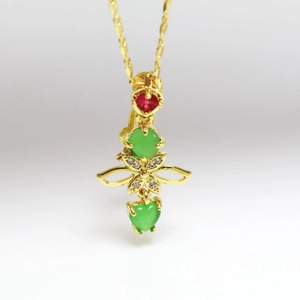 Detail eines Goldanhängers mit rotem Herz-Edelstein und grünen Kristallen an feiner Kette