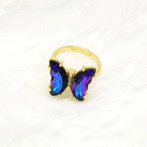 Nahaufnahme eines goldenen Schmetterlingsrings mit blauem Kristall und offenem Band