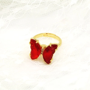 Detail eines verstellbaren Goldrings mit rotem Kristall-Schmetterling auf Spitzenstoff