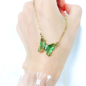 Detailed view of a green crystal butterfly pendant with sparkling rhinestones on a gold chain