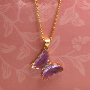 Dettaglio di una collana dorata con pendente a farfalla in cristallo lilla e pietrine