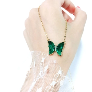 Detail of a gold butterfly necklace featuring dark green faceted crystal wings and zircons