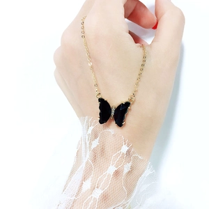 Detail of a gold-tone necklace with a black butterfly pendant held by hand with lace
