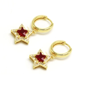Détail de créoles dorées avec pendentifs étoiles, pierre rouge et petits cristaux
