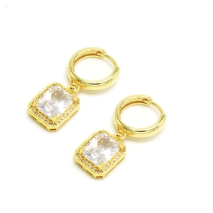 Détail de boucles d'oreilles créoles dorées avec zircon rectangulaire et pavage de cristaux