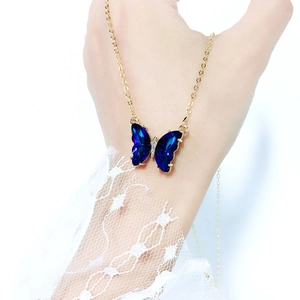 Close-up of a blue crystal butterfly necklace on a gold chain with lace sleeve detail