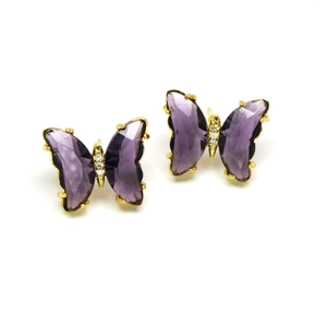 Macro detail of butterfly stud earrings featuring purple crystal wings in gold plating