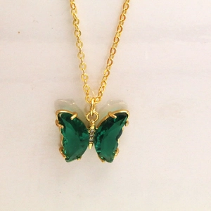 Détail d'un pendentif papillon doré avec des pierres vertes et des zircons blancs