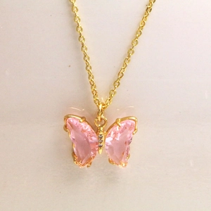 Détail d'un collier papillon avec des ailes en cristal rose et une chaîne dorée