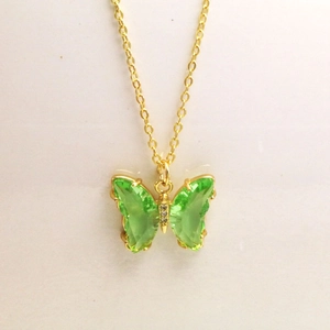 Détail d'un pendentif papillon doré avec des ailes en cristal vert et de petits diamants