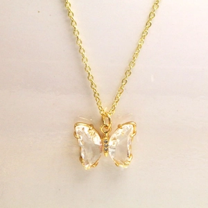 Détail d'un collier papillon doré avec des ailes en cristal facetté et une chaîne fine