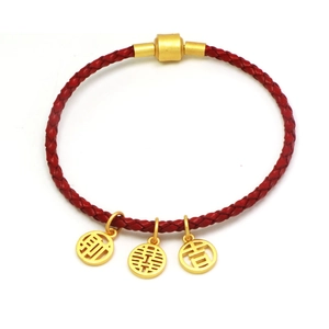 Detailed view of woven red cord bracelet with gold Fortune, Joy, and Luck charms