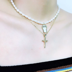 Detailopname van dubbele ketting met parelmoer slipper hanger en gouden kruisje