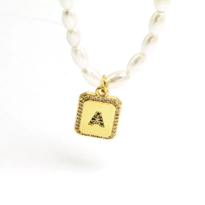 Detail of pearl necklace with gold letter A pendant featuring multicolored gemstones