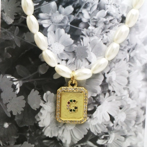Macro detail of pearl necklace featuring a gold pendant with crystal letter G inlay