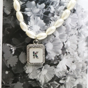 Detailed close-up of a pearl necklace featuring a rectangular letter K pendant with gems