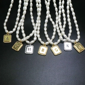 Macro detail of rice pearl necklaces featuring gold pendants with colorful gemstone letters