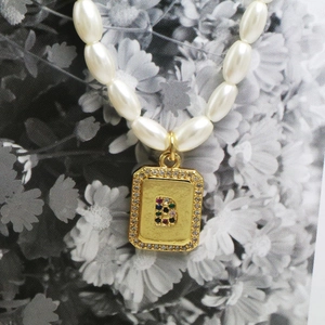 Detailed macro view of an oval pearl necklace featuring a gold letter B pendant with gems