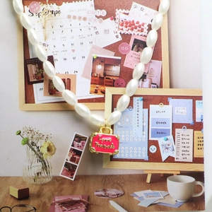 Detail van de parelketting met roze emaille kofferhanger en Love Travels inscriptie
