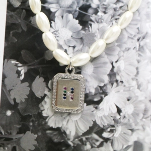 Macro view of pearl necklace featuring a silver pendant with colorful gemstone letter H