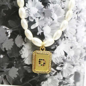 Close-up of pearl necklace with gold rectangle pendant featuring a diamond letter D