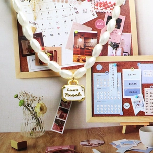 Detail van parelketting met gouden Love Travels kofferhanger voor dames