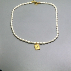 Detailed view of pearl necklace featuring a gold rectangle pendant with a crystal letter A
