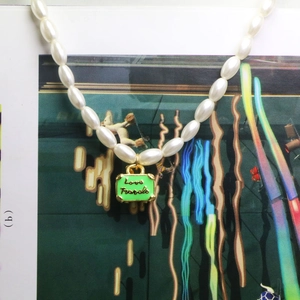 Detailopname van parelketting met groene Love Travels kofferhanger in macro