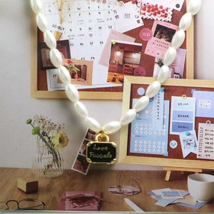 Detail van parelketting met Love Travels emaille hanger op een creatieve achtergrond
