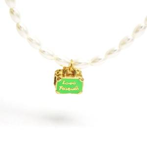 Detail of white oval pearl necklace featuring a gold suitcase pendant with Love Travels text