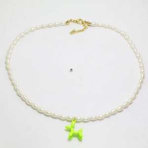 Détail de perles ovales blanches et d'un pendentif chien ballon vert sur collier doré
