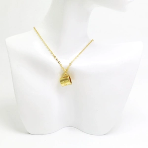Détail d'un collier doré avec un pendentif en forme de tasse et gravure CO sur un mannequin