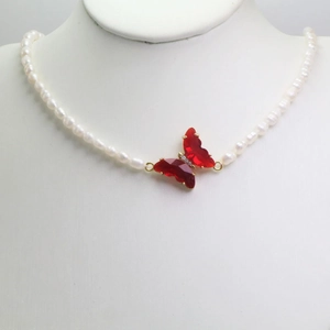 Detalle del collar de perlas naturales con colgante de mariposa de cristal rojo