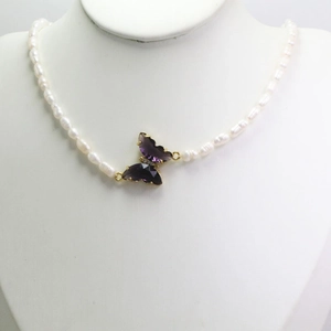 Detalle de collar de perlas naturales con colgante de mariposa en cristal púrpura