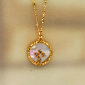 Detalle de collar de cruz de nácar con circonitas en colgante redondo dorado