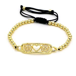 Detalle de la pulsera de cuentas doradas con colgantes de caritas y cordón negro