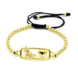 Detalle macro de los dijes de libélula dorada y corazón en una pulsera de cordón trenzado