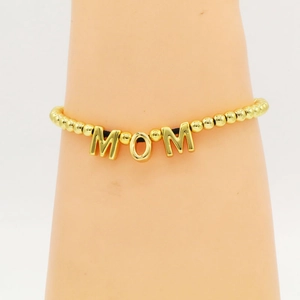 Close-up of golden beaded bracelet featuring a Mom letter charm for Mother's Day