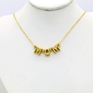 Detailed view of gold Mama necklace with polished finish on a white jewelry display stand